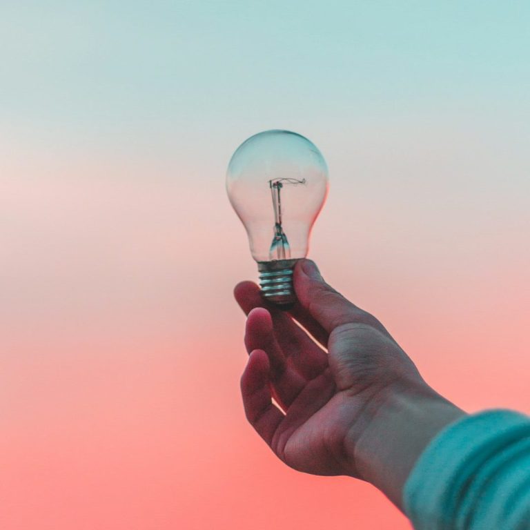 Neue Perspektiven Eine Hand hält eine Glühbirne vor einem pastelfarbenen Hintergrund.